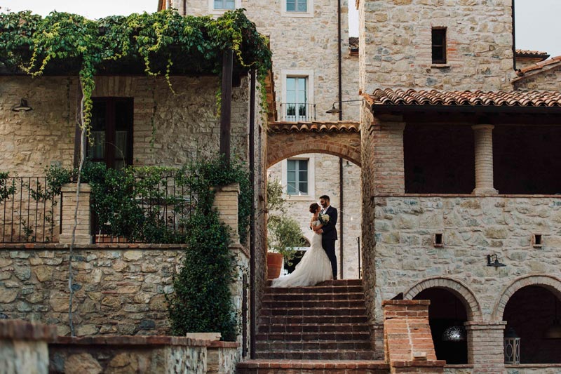 In questa foto una coppia di sposi in posa sotto un arco, tra le case del borgo medievale per matrimoni in Umbria Spao Borgo San Pietro