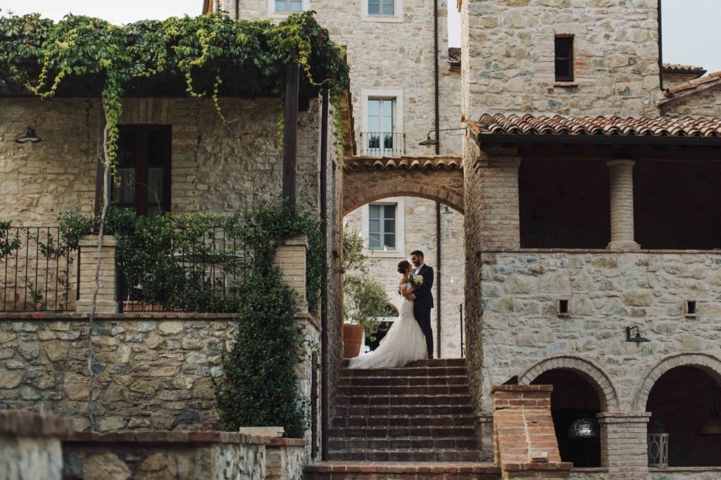 In questa foto una coppia di sposi sotto un arco tra le antiche case di Borgo San Pietro, location per matrimoni di lusso in Toscana