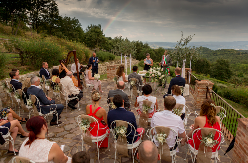 In this photo the guests of a wedding sitting on one of the terraces in the garden of spao borgo san pietro, while they attend the wedding ceremony with a civil ceremony